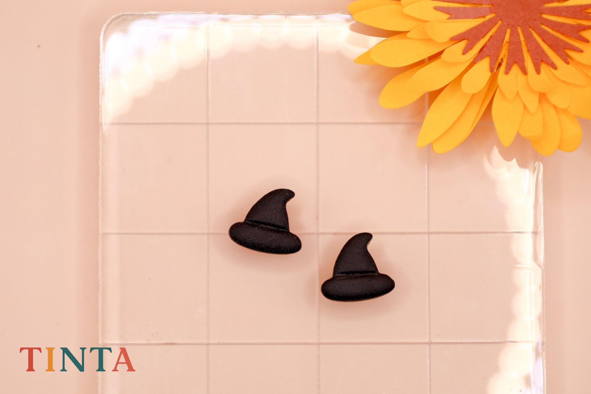 Black witch hat earrings on a pink surface with a yellow flower.