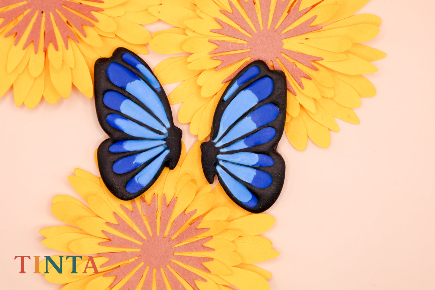 Blue butterfly wings on yellow flowers with 'TINTA' branding