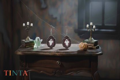 Halloween-themed earrings on a wooden table with ghost and candle decorations, featuring the brand 'TINTA'.