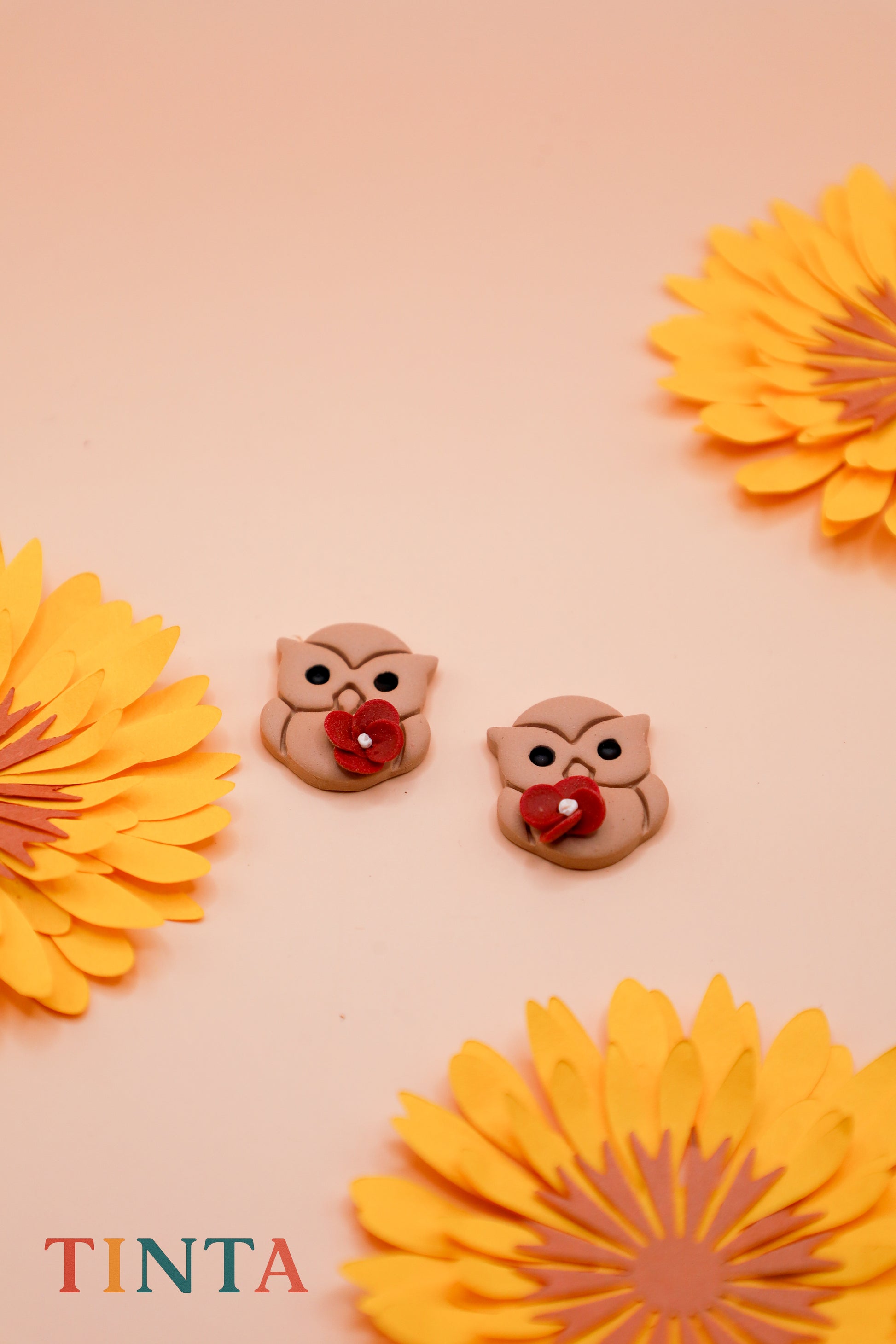 Two owl-shaped buttons with red centers on a beige background with yellow flowers.